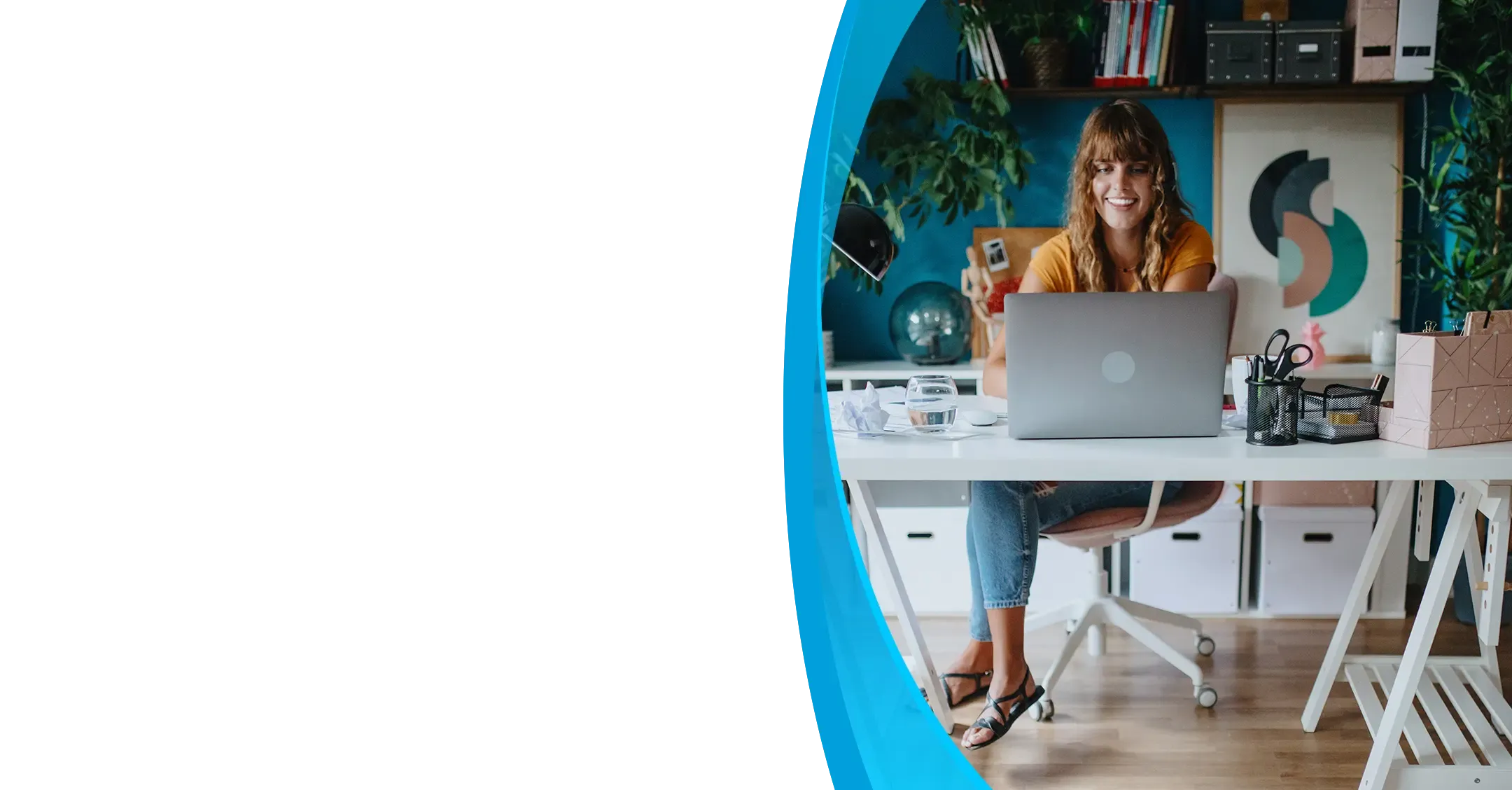 A smiling woman works on a laptop at a white desk while a black dog rests on a rug nearby.